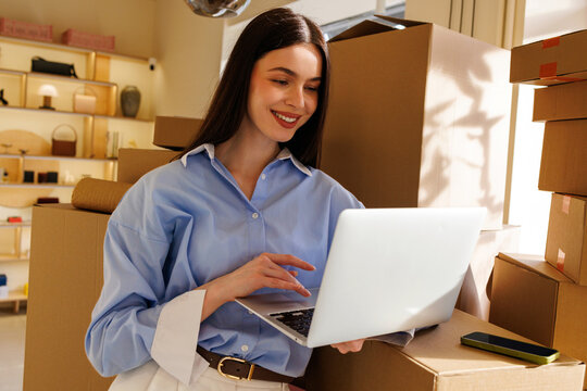 Woman using laptop among boxes in small business workspace