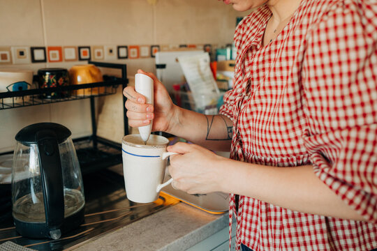 Woman using handheld milk frother in mug in kitchen