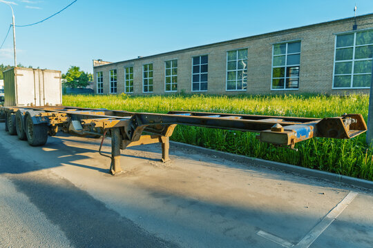Empty multi-axle container chassis parked by industrial building at sunset