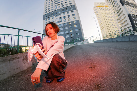 Young Person Holds Phone While Standing in Urban Area at Sunset