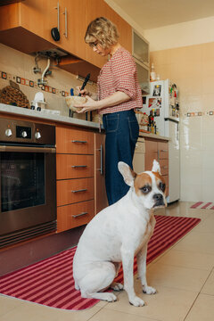 Woman preparing meal in kitchen while dog sits nearby