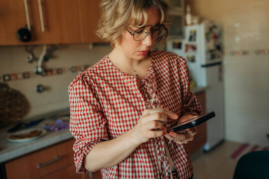 Woman using smartphone in kitchen ordering groceries online