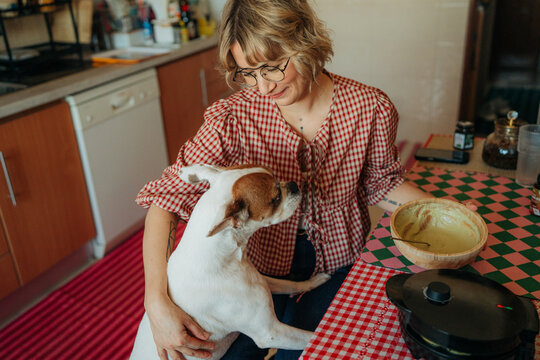 Woman petting dog while preparing waffles in kitchen