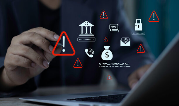 Businessman using laptop with bank fraud warning hologram. Financial scam detection and cybersecurity alert icons on money, email phishing, and phone risk.