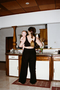 Woman holds baby in kitchen while preparing food