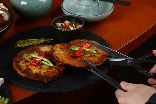 Hands using scissors and tongs to cut a crispy Korean mung bean pancake 가위와 집게를 사용하여 바삭한 한국식 녹두전을 자르는 손길