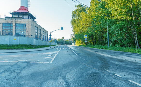 Empty urban road with industrial building and leafy trees at dawn