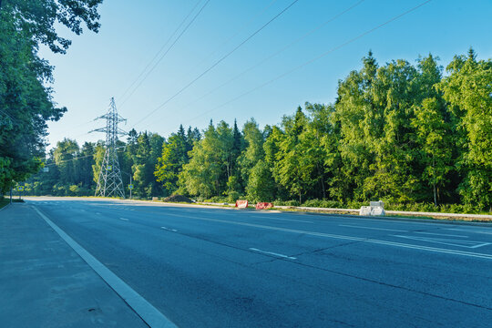 Empty suburban highway bordered by green forest and utility pylon