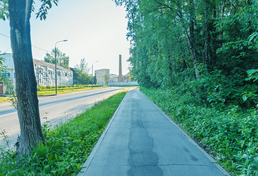 Quiet suburban sidewalk bordered by green trees and industrial buildings