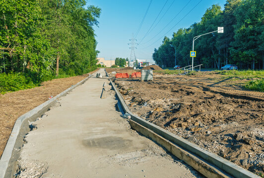 Newly poured concrete sidewalk under construction alongside a wooded roadside
