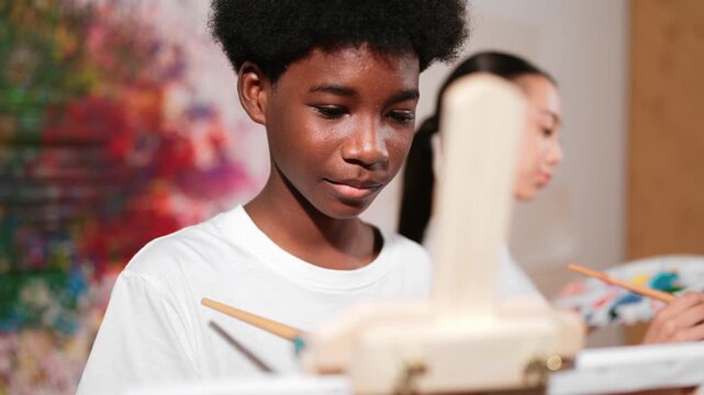Smart african boy painting canvas while cute girl drawing behind. in art lesson. high school student create artwork by express creativity idea while standing at colorful stained wall. Edification