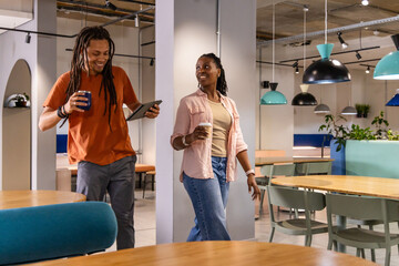 African American coworkers walking, chatting in lounge with casual wear, tablet, mug and paper cup © wavebreak3