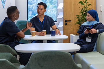 Obraz premium Diverse coworkers in navy scrubs sitting in staff break room, gesturing, holding coffee, phone, ID