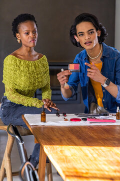 Diverse makeup artist and client discussing dual-shade palette at wooden table with brushes