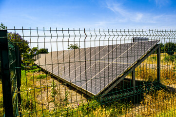 Fototapeta premium Photovoltaic solar panels in a countryside near highway surrounded by fence under sunny blue sky, renewable energy carbon footprint reduction