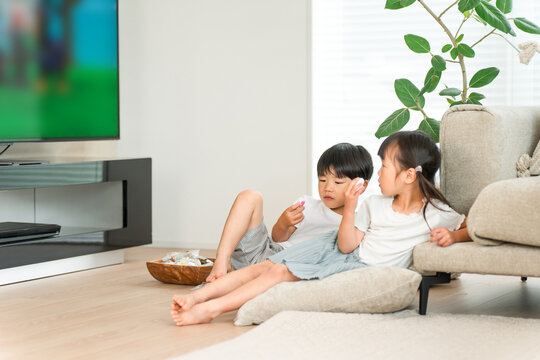 A close brother and sister eating snacks while watching TV and anime on the living room sofa.
