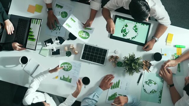Top down view of business team discussing about using clean energy and sustainable investment at meeting table with wind mill, document with environmental graph and wooden house model. Alimentation.