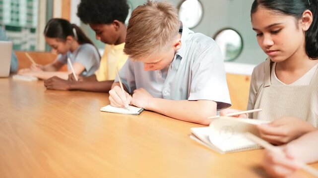 Smart student with mixed races doing test while caucasian teacher using laptop analysis data. Young happy high school boy writing or taking a note at classroom. Creative education concept. Edification