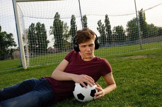 Handsome teen laying on the grass on soccer field with soccer ball waring headphones 