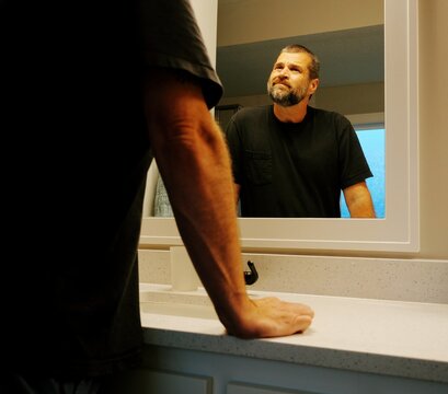 Middle aged man taking daily vitamins prescription medicine pills bathroom mirror routine healthy aging healthcare compliance self care grooming