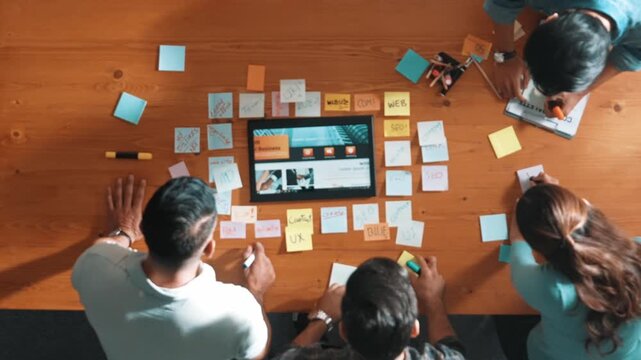 Top view of business people working together to design web design. Aerial view of designer brainstorming and discussing about website interface and looking at tablet with digital design. Symposium.