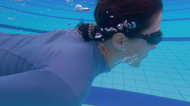 Athletic sportswoman practicing underwater swimming in deep outdoor pool. 