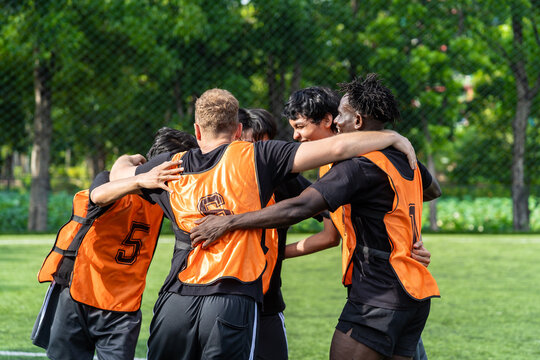 Group of male football players hugging in a team circle on outdoor field.