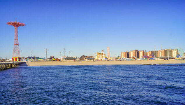 Coney Island panorama in Brighton Beach, New York City, with Atlantic shoreline, amusement rides, and the Parachute Jump tower.
