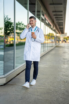 Male doctor walking, talking on phone, drinking coffee