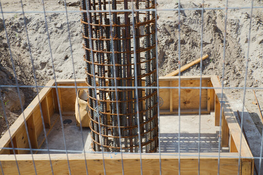 Close-up of a building foundation under construction showing a cylindrical steel rebar cage set inside wooden formwork on a sandy construction site, illustrating reinforcement, engineering and industr