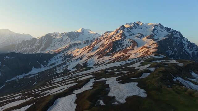 Cinematic dolly in aerial flying over rugged alpine terrain with melting snow patches toward snow covered Himalayan mountain peaks near Sar Pass Trek, Kasol, Himachal Pradesh, India.