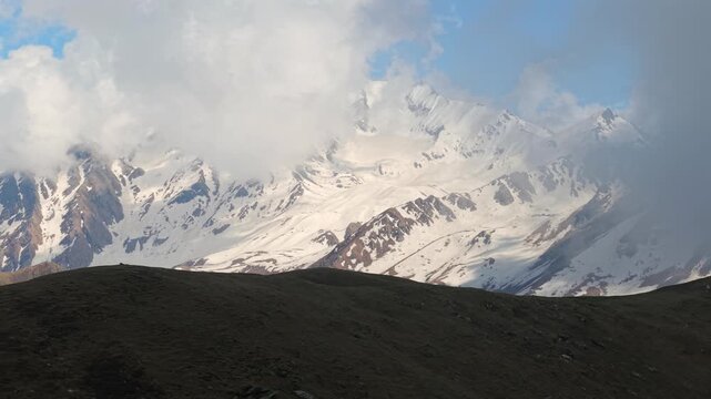Wide aerial view of snowcapped Himalayan peaks with clouds and rugged alpine terrain near Sar Pass Trek, Parvati Valley, India.