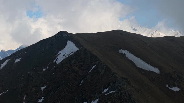 Aerial close up view of rugged alpine ridge with snow patches and clouds in Himalayan mountains near Sar Pass Trek, Parvati Valley, India.