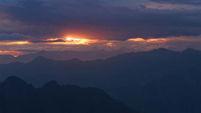 Himalayan mountain ridges with glowing sunset light breaking through dense clouds near Parvati Valley in Himachal Pradesh, India. Cinematic aerial landscape