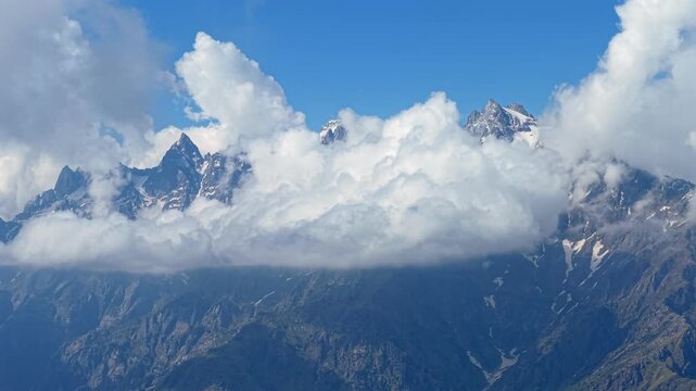 Static aerial shot Himalayan mountain peaks partially hidden beneath rolling clouds and snow covered summits near Sar Pass Trek and Parvati Valley, India