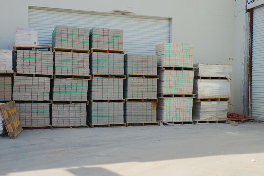Neatly stacked pale bricks secured with green strapping on a wooden pallet at a construction supply yard, ideal for masonry, paving and building projects; outdoor industrial storage of building materi