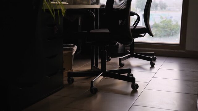 Cinematic low angle shot of an empty modern office workspace with black mesh chairs and natural daylight through a large window. Ideal for corporate background b-roll.