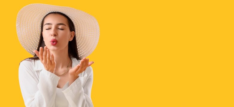 Young woman in straw hat blowing kiss with closed eyes, summer vacation and travel concept, isolated on yellow background