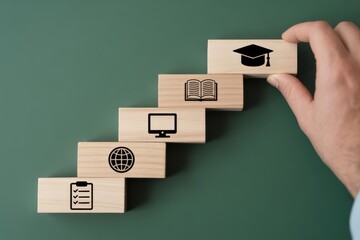 Hand stacking wooden blocks with education icons on green background