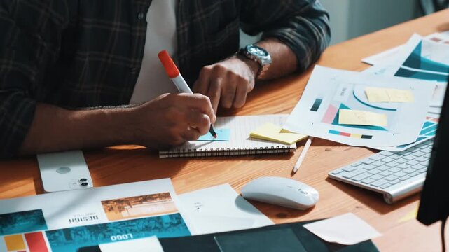 Professional designer writing and designing logo graphic at meeting. Closeup of business man working on colored palettes and writing idea on sticky notes on table with equipment and paper. Symposium.