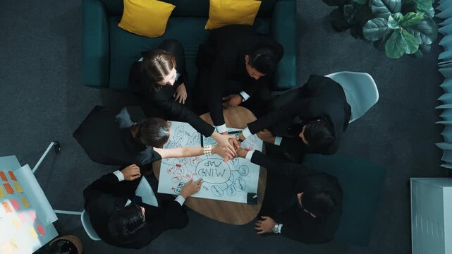 Top down aerial view of people putting hands together and clapping hands to celebrate successful project while using mind map to brainstorm idea. Skilled team stacking hands together. Directorate.