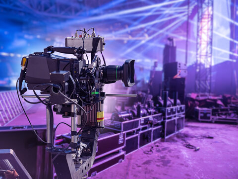 Live event production. Professional video camera records concert stage with lighting equipment and broadcast setup.
