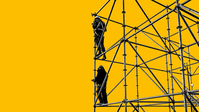 Scaffolding construction. Workers in safety harnesses climb metal framework during high rise installation and maintenance.