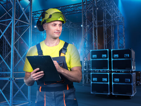 Event production. Stage technician checks equipment and truss structures with clipboard before lighting and concert setup.