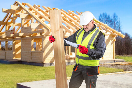 Timber construction. Building inspector checks wooden beam and plans near house frame during residential carpentry work.