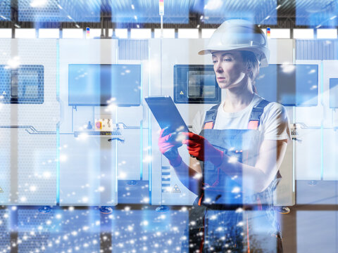 Smart manufacturing. Female technician operates tablet interface near automated CNC machines in a high tech factory.