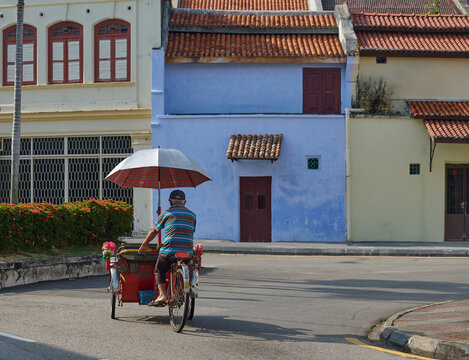 Traditional trishaw rider cycling past Nanyang heritage houses in George Town, Penang, Malaysia