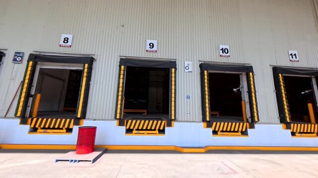 Panning View of Seven Open Loading Docks at Distribution Center. Distribution Center Loading Docks Viewed from Truck Yard. Warehouse Shipping and Receiving Area with Open Dock Doors