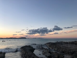 Obraz premium Rocky shoreline with distant city skyline at sunset