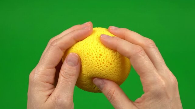 Close up view of human hand gently squeeze soft textured yellow foam stress ball sponge on bright solid green screen background showing sensory touch with calm focus for mental tension relief